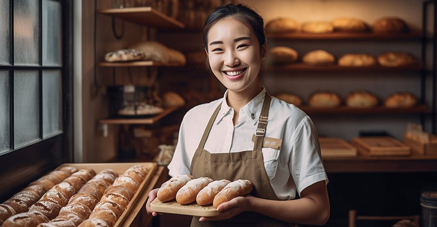 Women in a bakery smiling and holding a tray of bread rolls