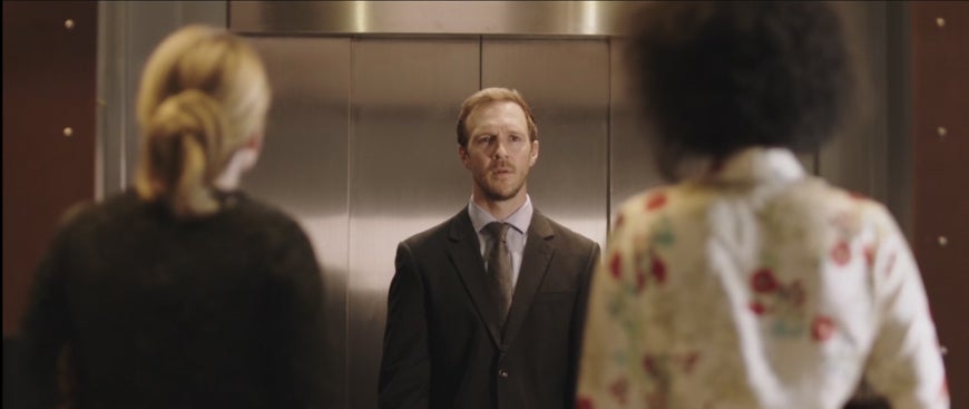 man starting at two women outside an elevator